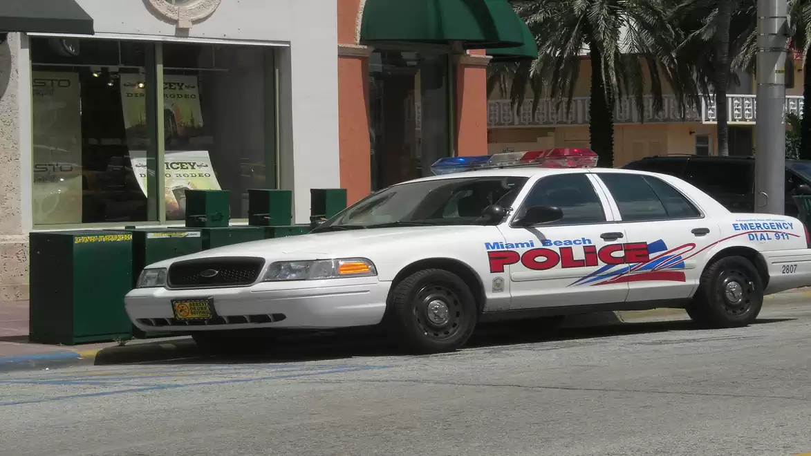 A white police car with the 'Miami Beach Police' inscription is parked in front of a building.