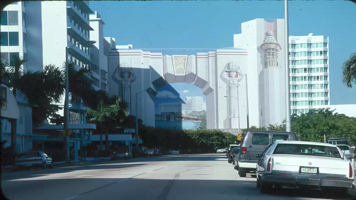 Street scene featuring modern buildings and cars heading towards an impressive building with large decorative architecture.