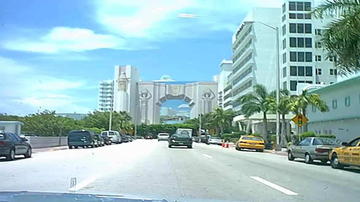 Street scene with modern buildings and palm trees in the background, blue sky.