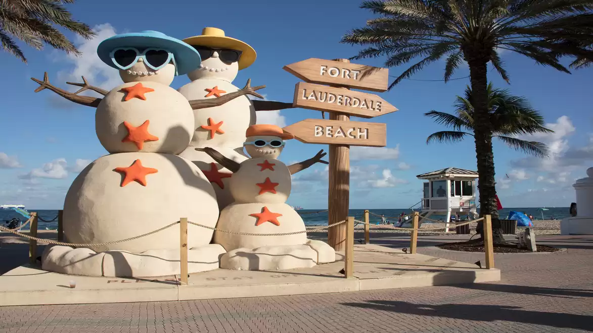 Beach scene with sand snowmen adorned with sunglasses and hats at Fort Lauderdale Beach.
