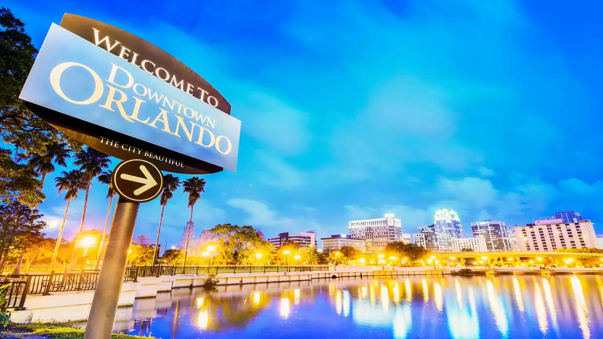 Welcome sign of Downtown Orlando at night, surrounded by illuminated cityscape and reflecting water.