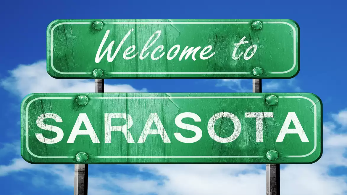 Green road sign with the inscription 'Welcome to Sarasota' against a blue sky with white clouds.