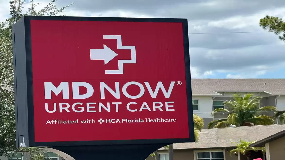 A sign for MD Now Urgent Care in front of a building complex with a slightly cloudy sky.