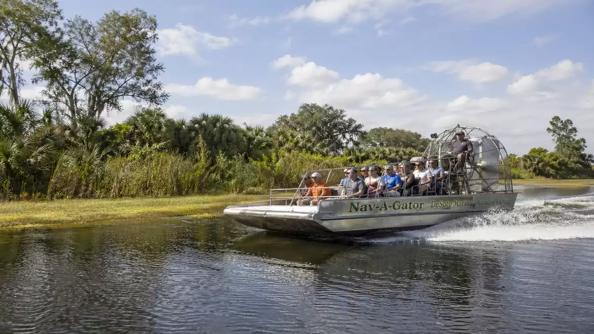 A group of people riding an airboat on a calm river through a lush, green landscape.