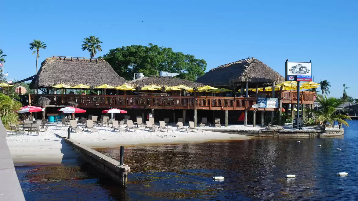 Beach restaurant with thatched roofs and colorful umbrellas on the shore of a body of water under a clear sky.