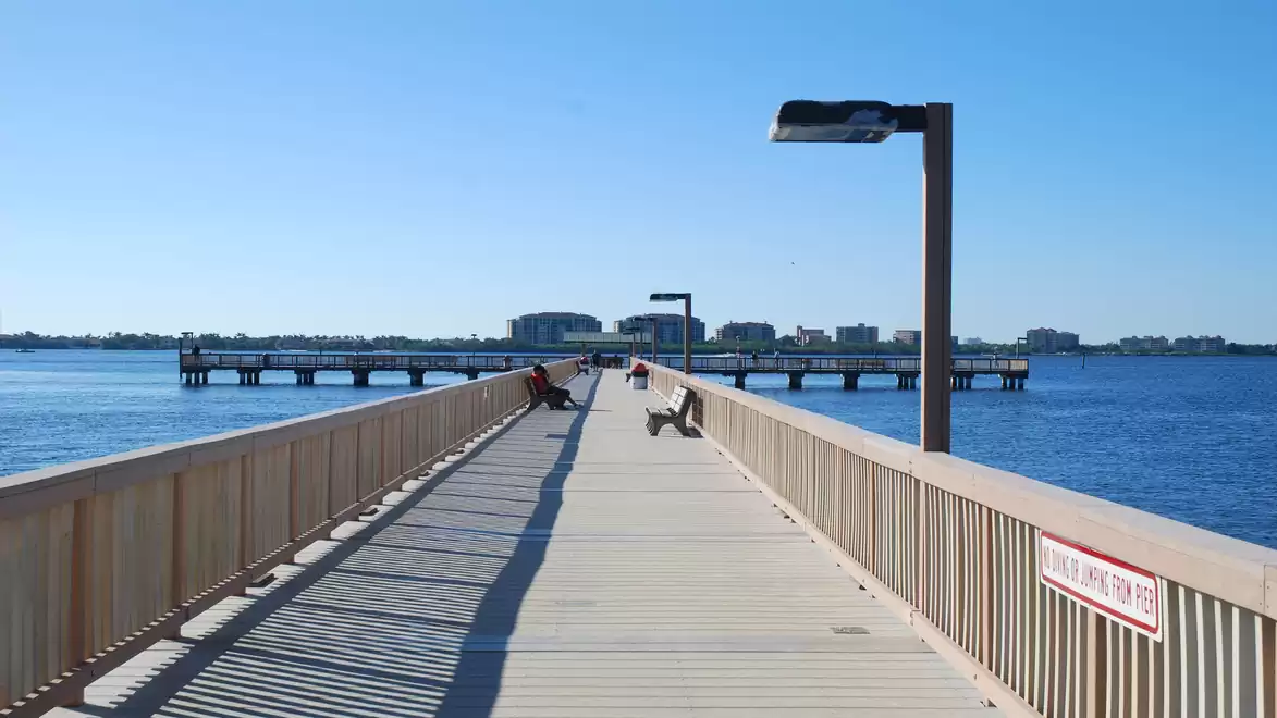 Long wooden pier leading out to blue water with people enjoying the view.