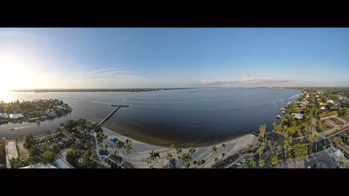 Panoramic view of a coastline with a beach, pier, and surrounding buildings at sunset.