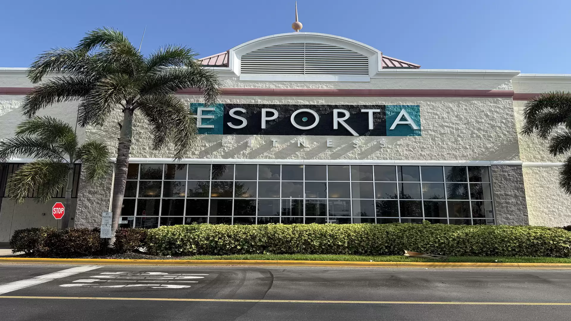 Exterior view of a gym called Esporta with large windows and palm trees.