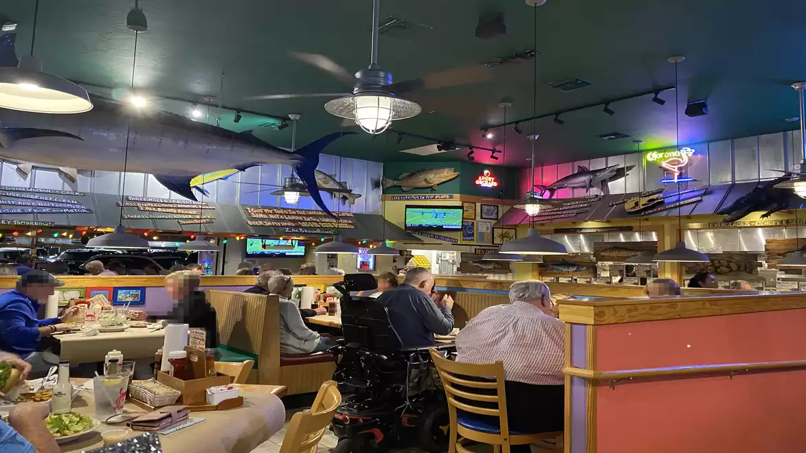 A busy restaurant with guests at tables, colorful lights, and fish decorations on the walls.