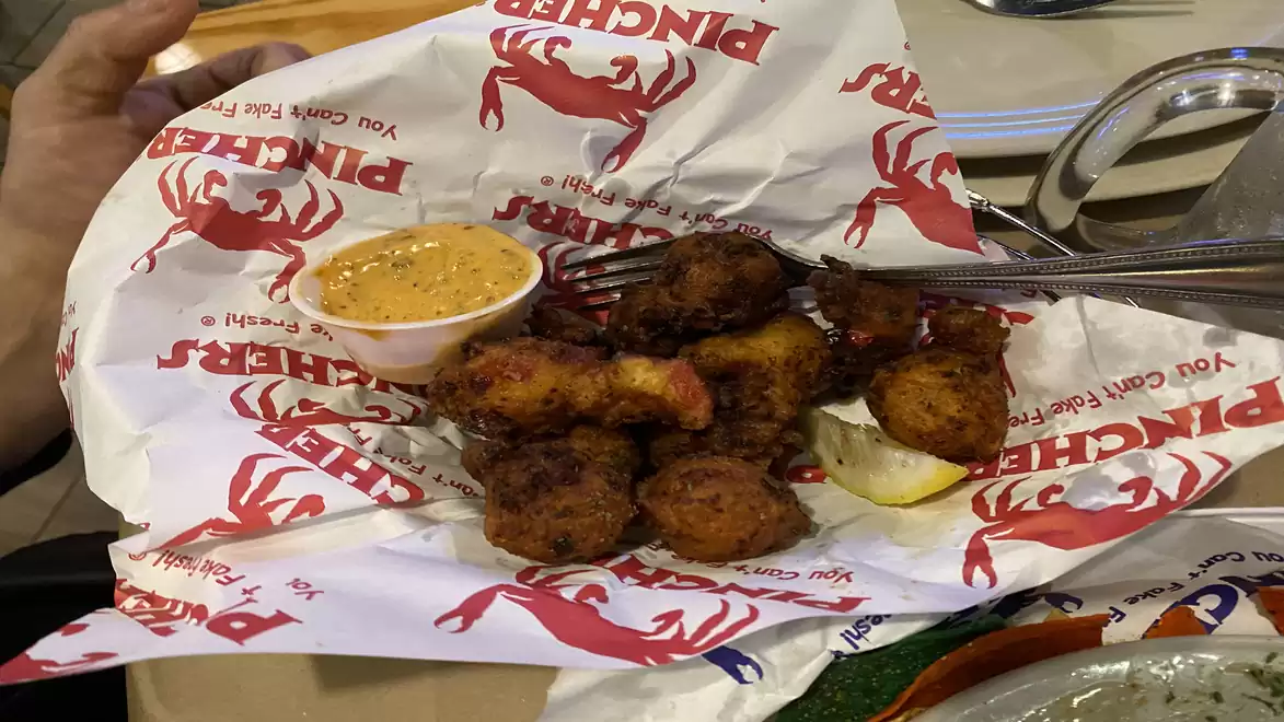 A plate of fried seafood on paper with a side of dipping sauce.