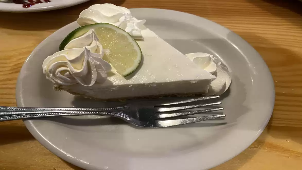 A slice of lime pie with cream on a plate, served with a fork.