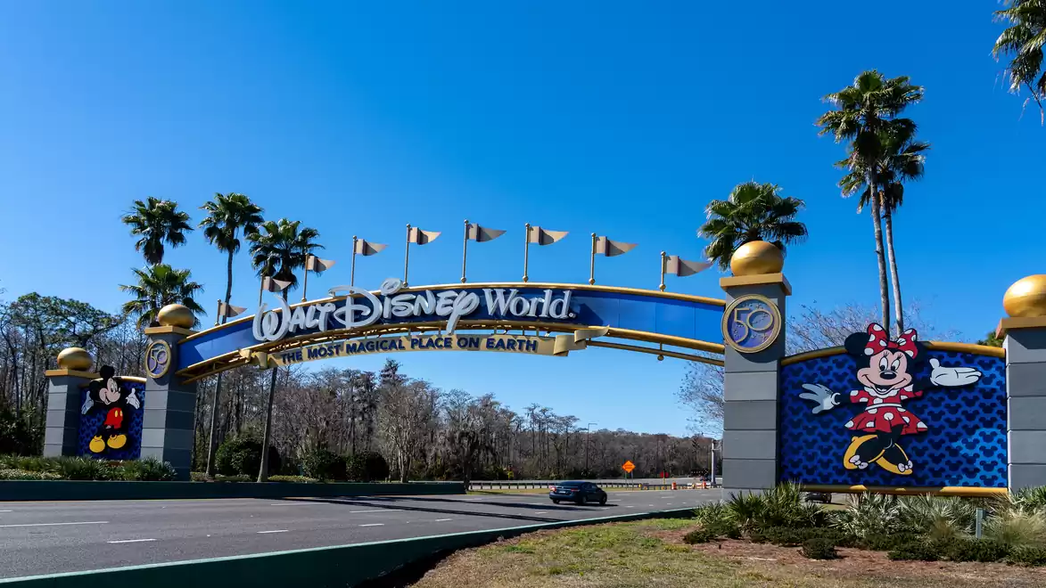 Entrance gate to Walt Disney World featuring Mickey and Minnie Mouse, surrounded by palm trees, under a blue sky.