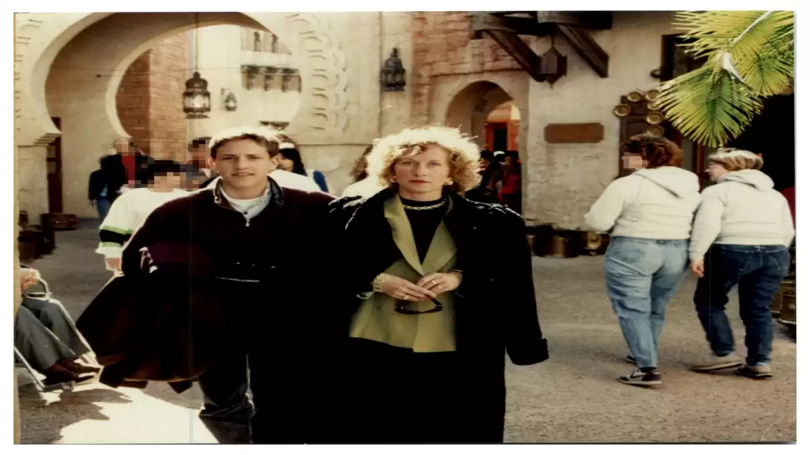 People walking through a busy courtyard with arches and old buildings.
