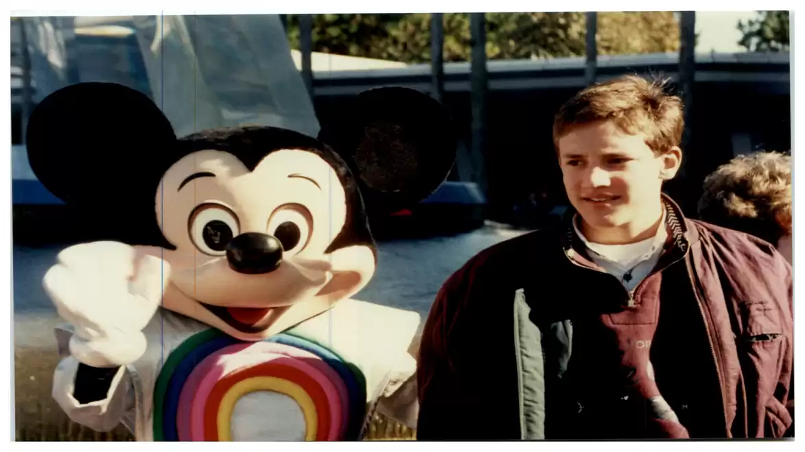 A person stands next to a figure dressed as a famous cartoon mouse with a rainbow cape.