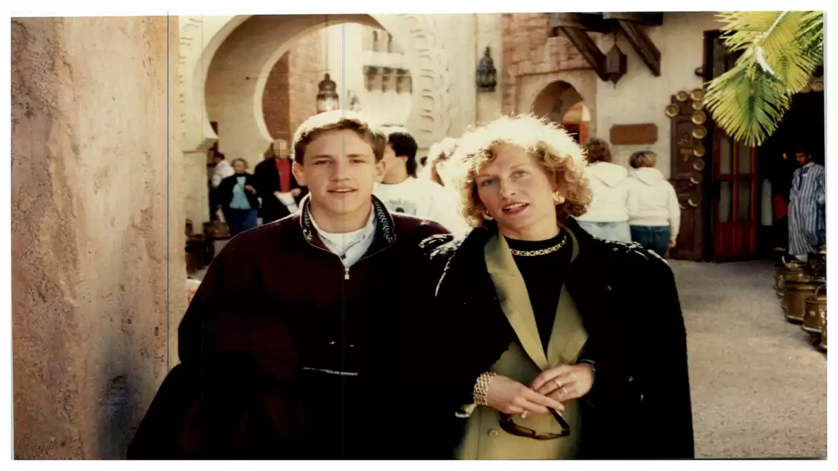 Two people standing in a sunny alley with historic buildings in the background.