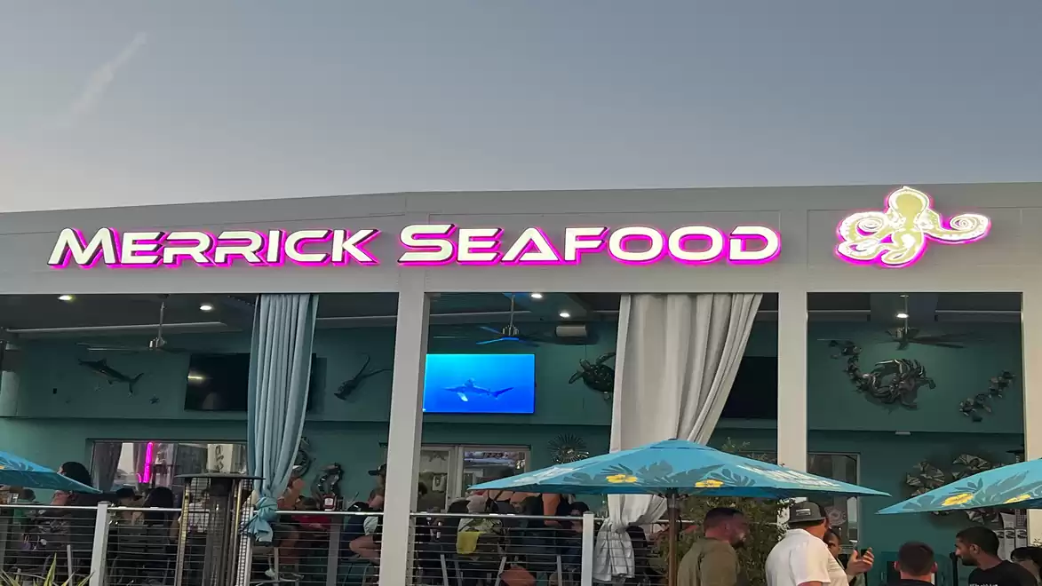 Exterior view of Merrick Seafood restaurant with illuminated sign and guests outside.