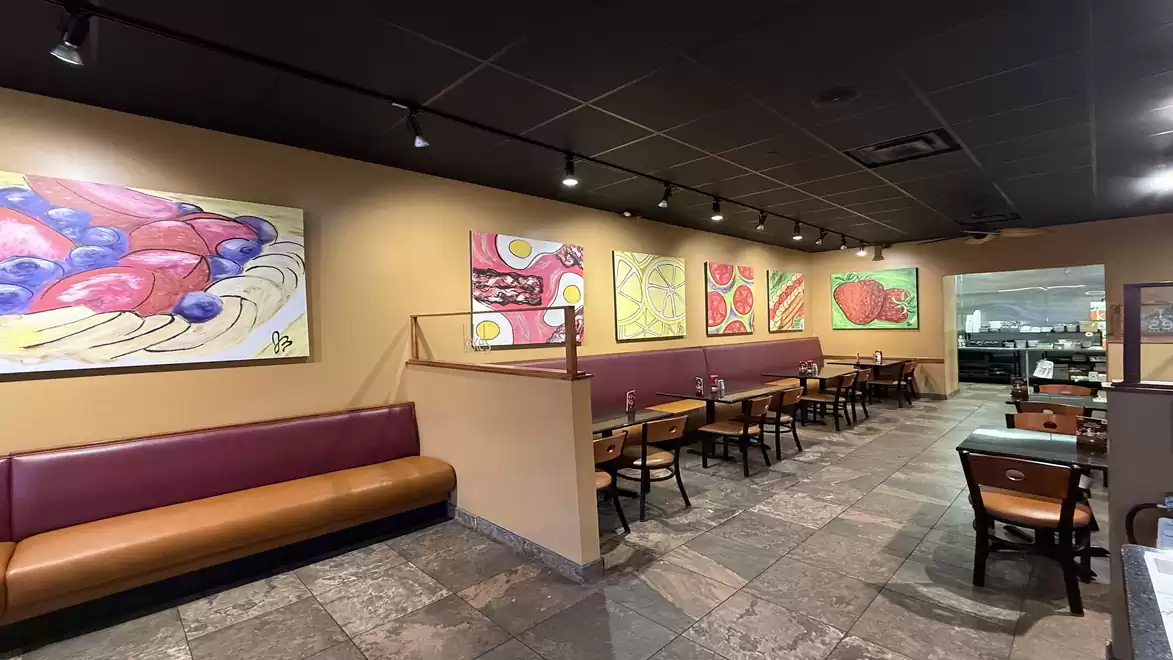 A modern restaurant with large, colorful paintings on the wall and red booths in a cozy atmosphere.