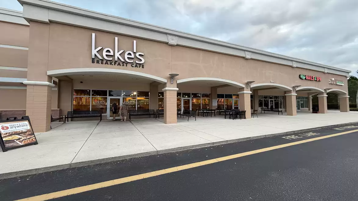 Exterior view of a shopping center with restaurants, including Keke's Breakfast Cafe and Subway, under a cloudy sky.