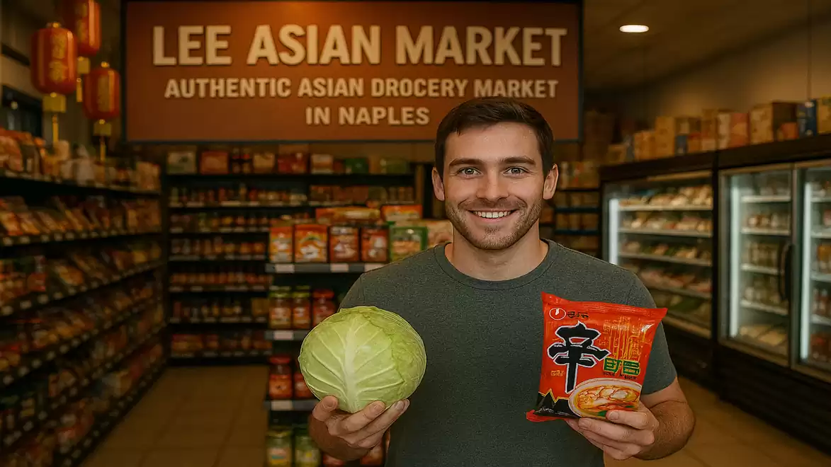 A smiling man stands in an Asian supermarket holding a cabbage and a package of instant noodles.