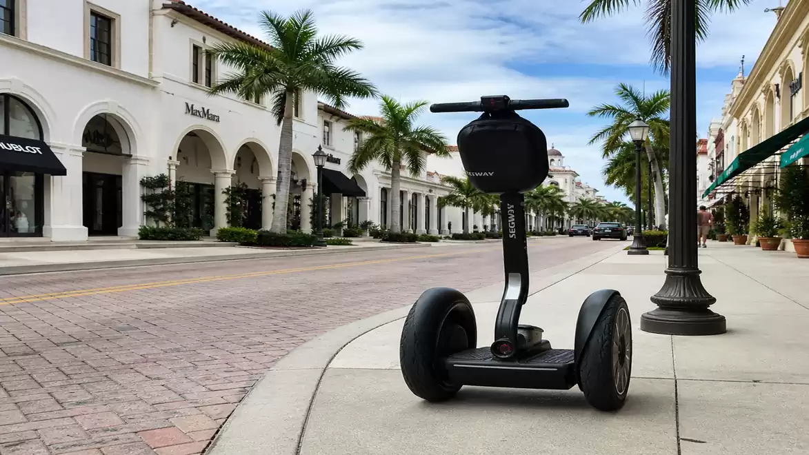 A Segway personal transporter on the sidewalk of a palm-lined shopping street with elegant buildings.