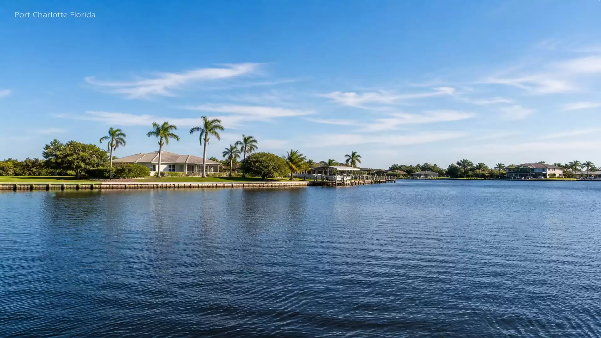 View of a tranquil residential area with palm trees by the water in Port Charlotte, Florida, under clear blue skies.