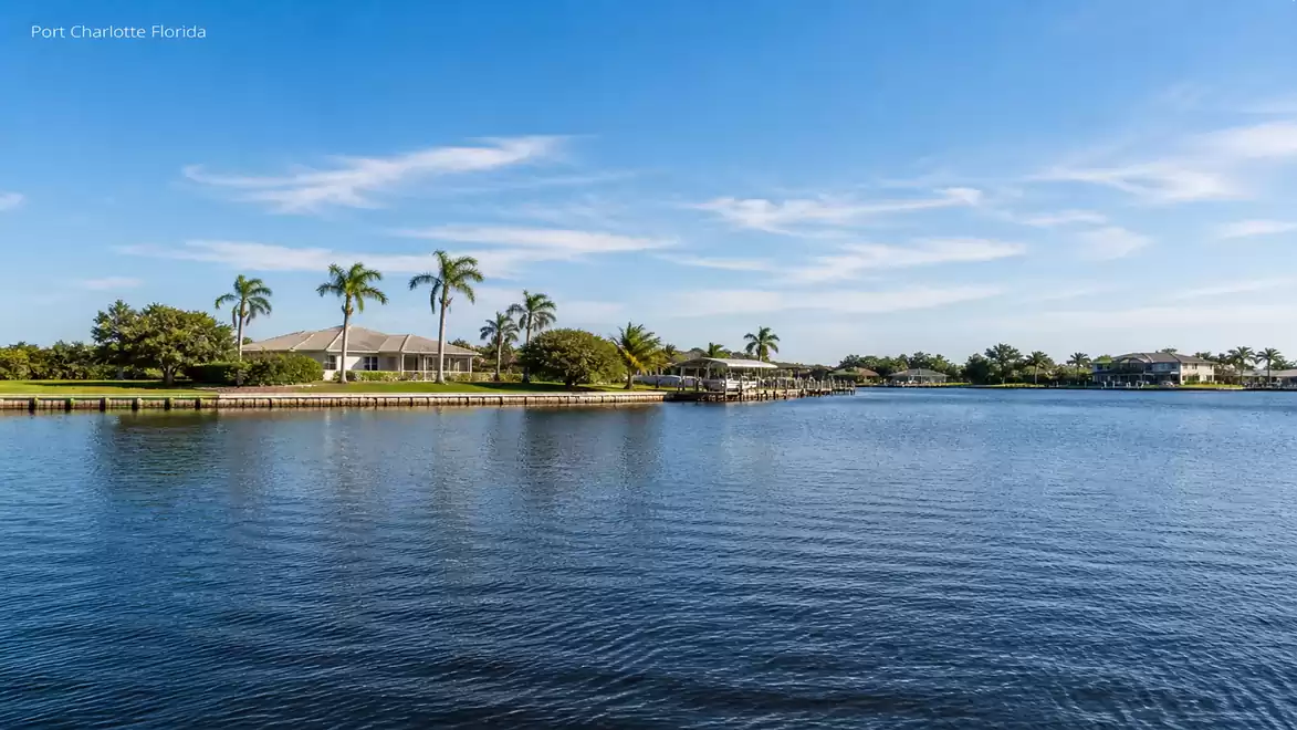 View of a tranquil residential area with palm trees by the water in Port Charlotte, Florida, under clear blue skies.