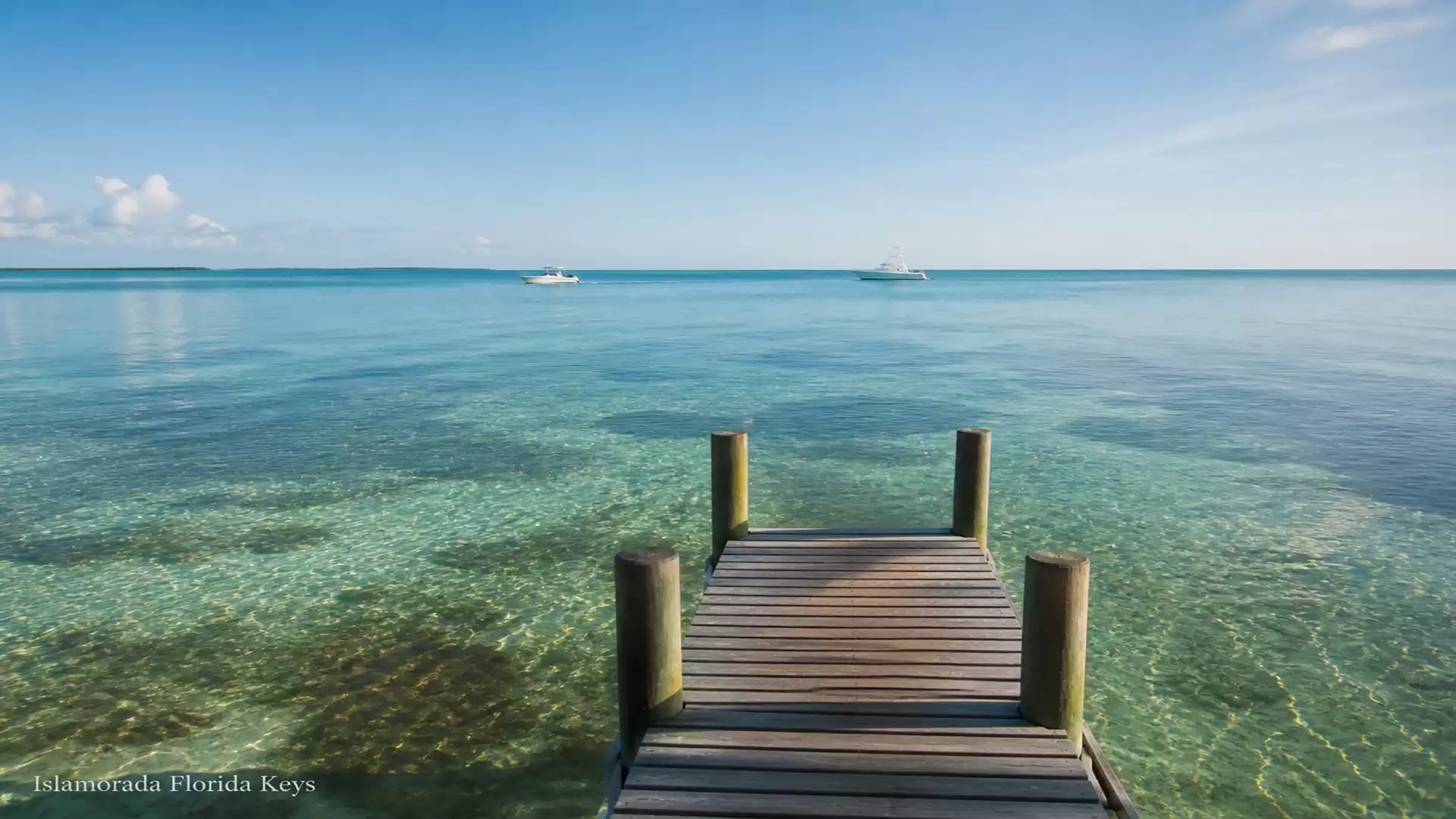 Wooden pier by the clear, blue sea in Islamorada, Florida Keys, with slightly cloudy sky.