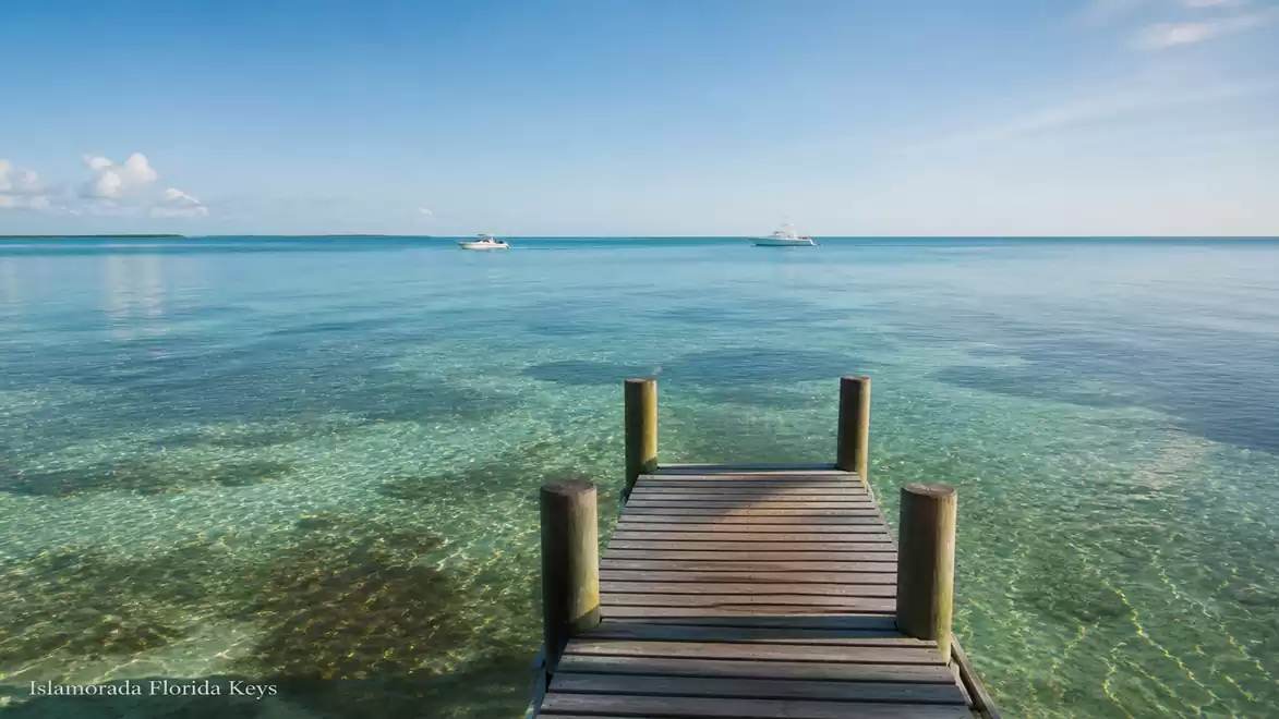 Wooden pier by the clear, blue sea in Islamorada, Florida Keys, with slightly cloudy sky.