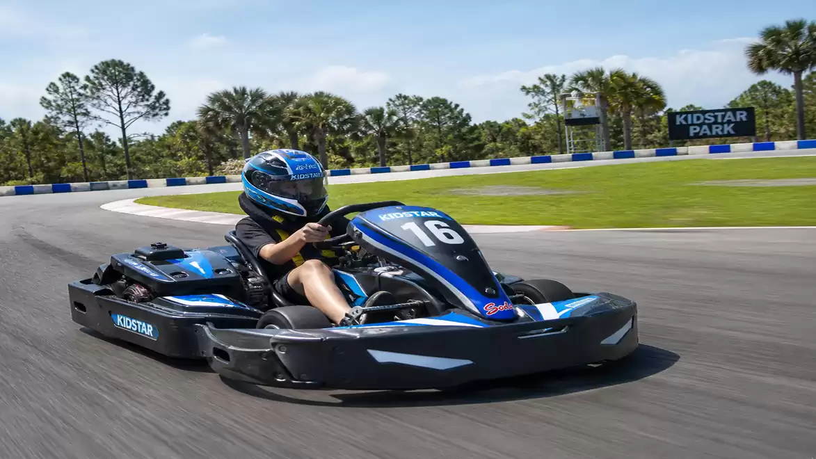 A person is driving a go-kart on a racetrack at Kidstar Park. It's sunny with a green environment and blue sky.