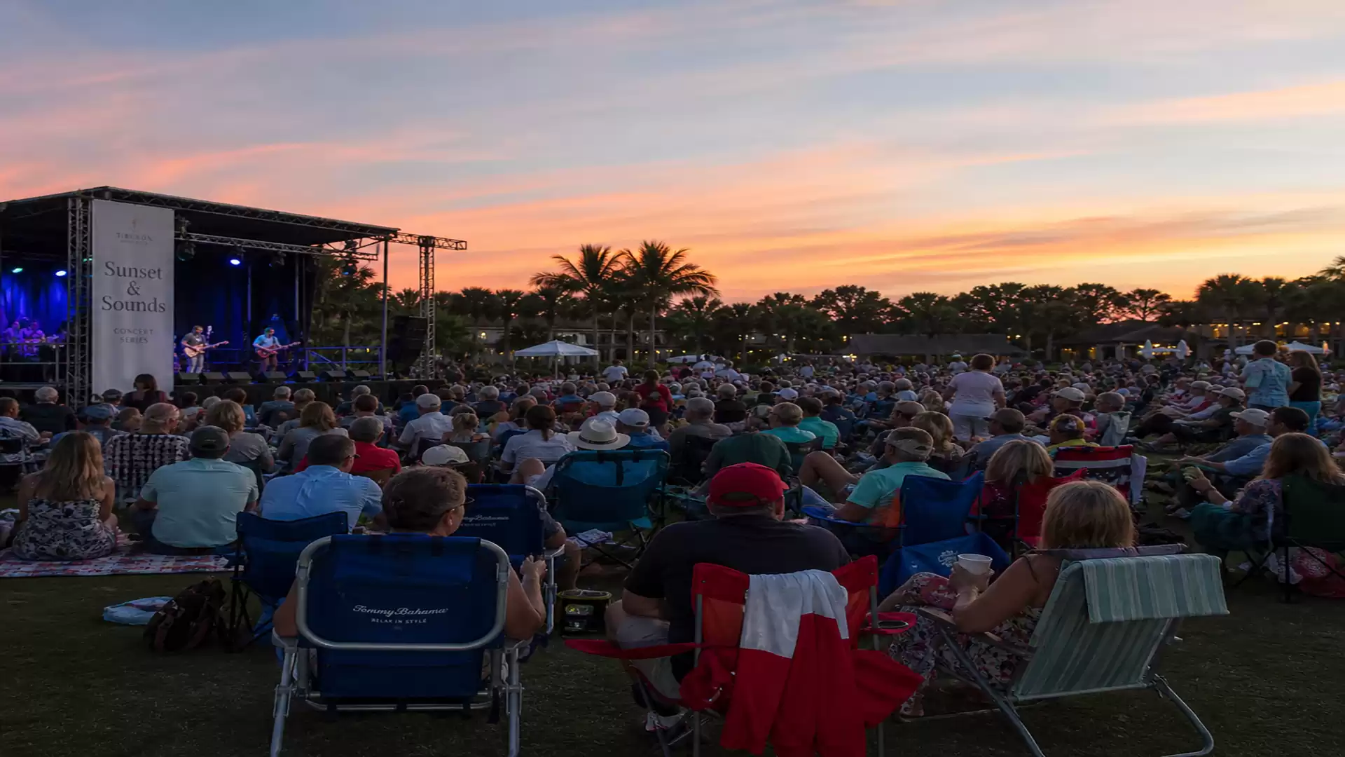 An outdoor concert at sunset with a large crowd of spectators in front of the stage.