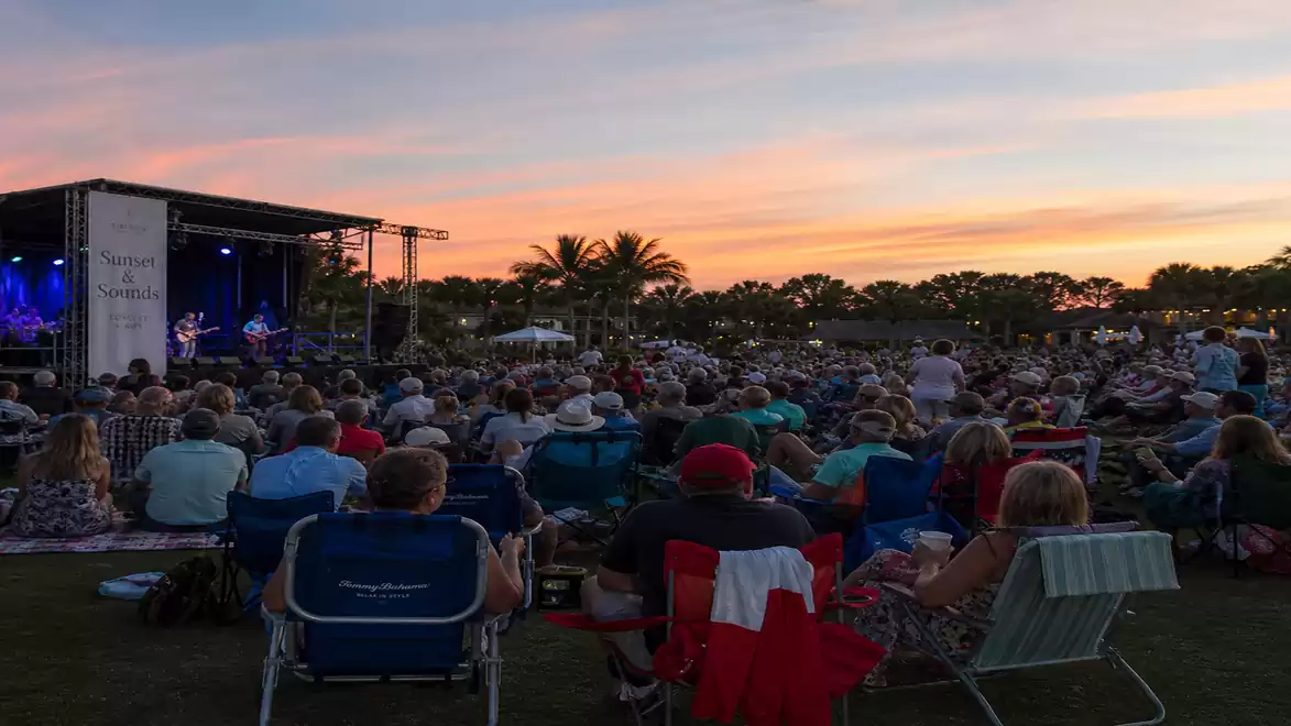 An outdoor concert at sunset with a large crowd of spectators in front of the stage.