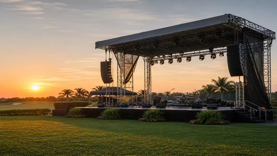 Outdoor stage at sunset with palm trees and a lawn.