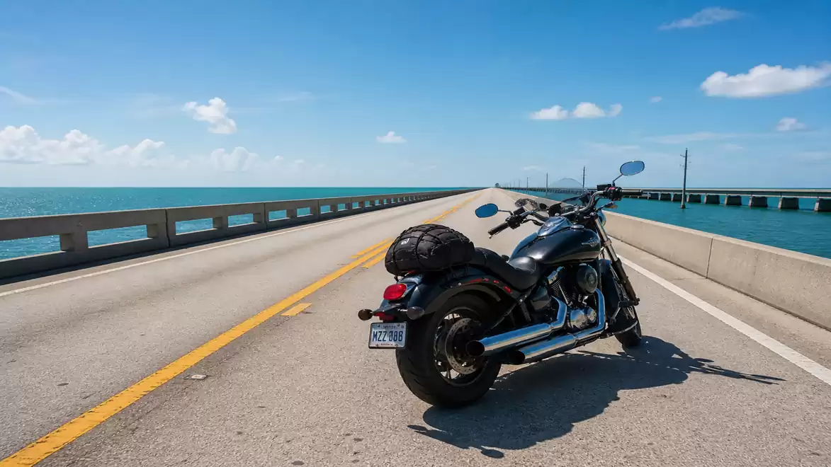 A motorcycle is parked on a long bridge over the ocean under a clear blue sky.