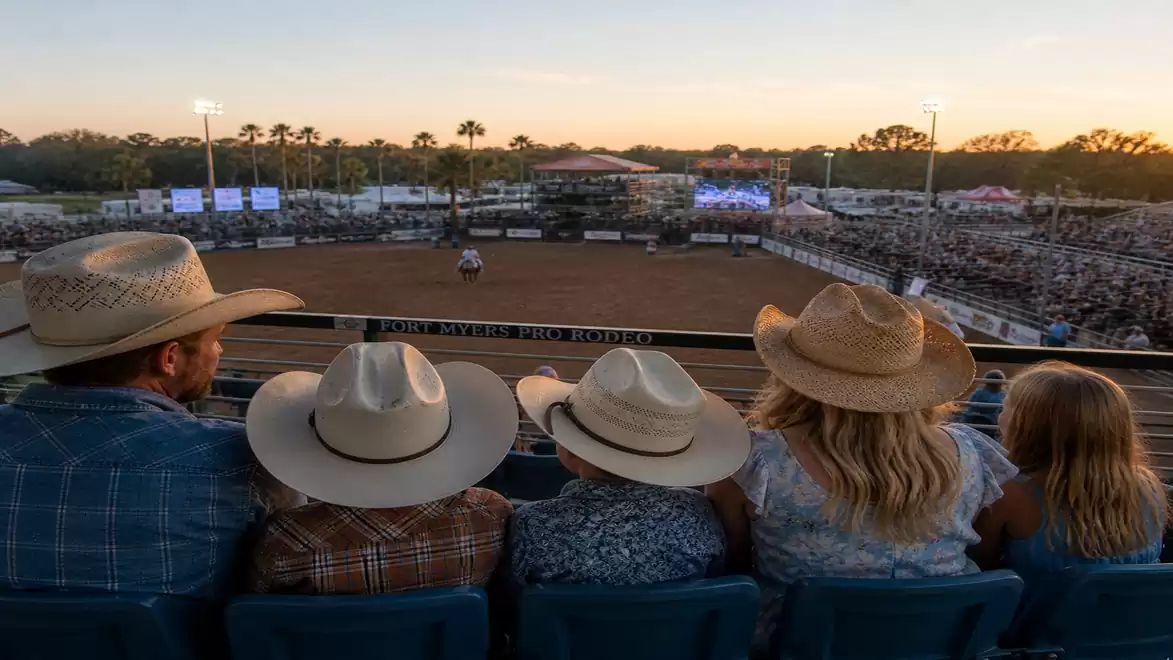 A family sits in a stadium watching a rodeo with a cowboy atmosphere at dusk.