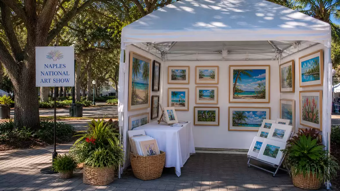 An art booth at the Naples National Art Show featuring various paintings of nature and the beach, surrounded by plants under a sunny sky.