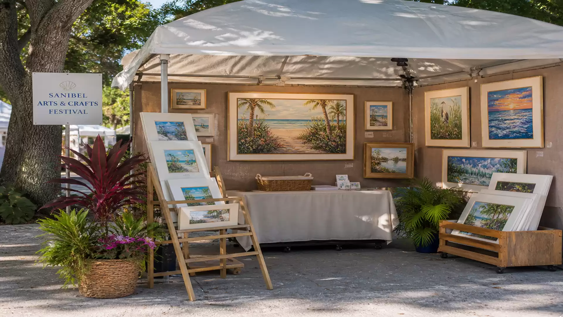 An art booth at a festival featuring landscape paintings under a white tent. Various artworks are decoratively displayed.