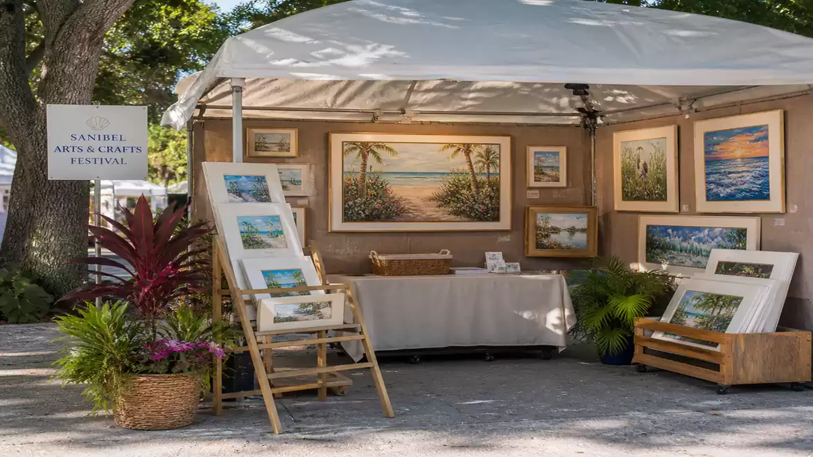 An art booth at a festival featuring landscape paintings under a white tent. Various artworks are decoratively displayed.