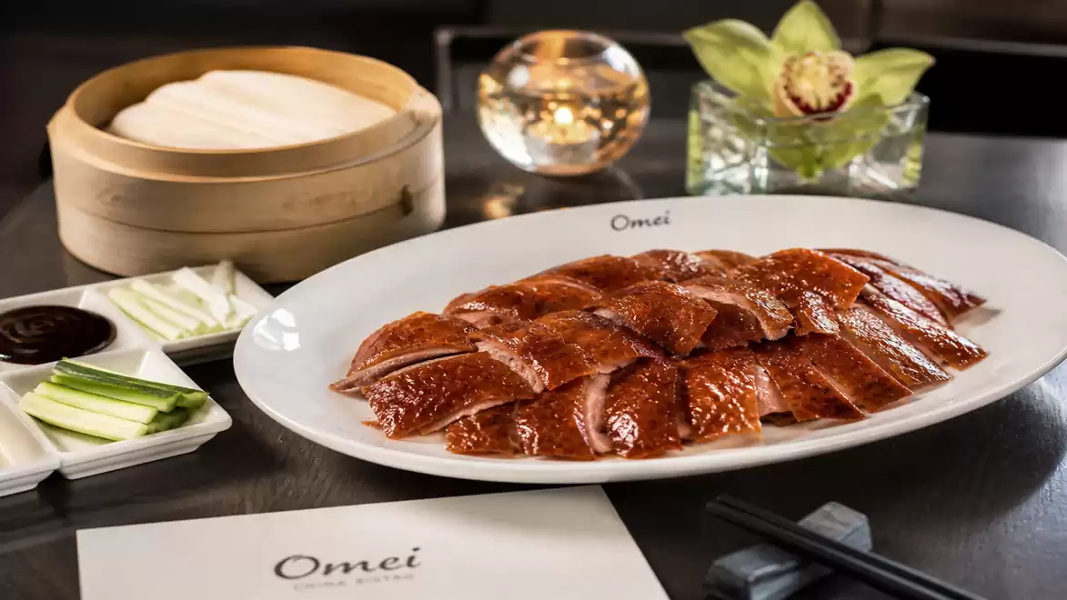 A plate of crispy duck with spices and steamed buns in a restaurant.
