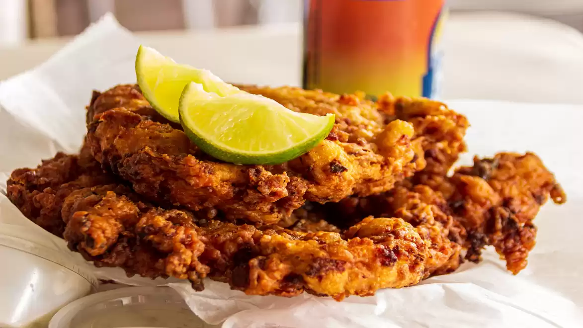Crispy fried chicken pieces served with lime slices, a can in the background.