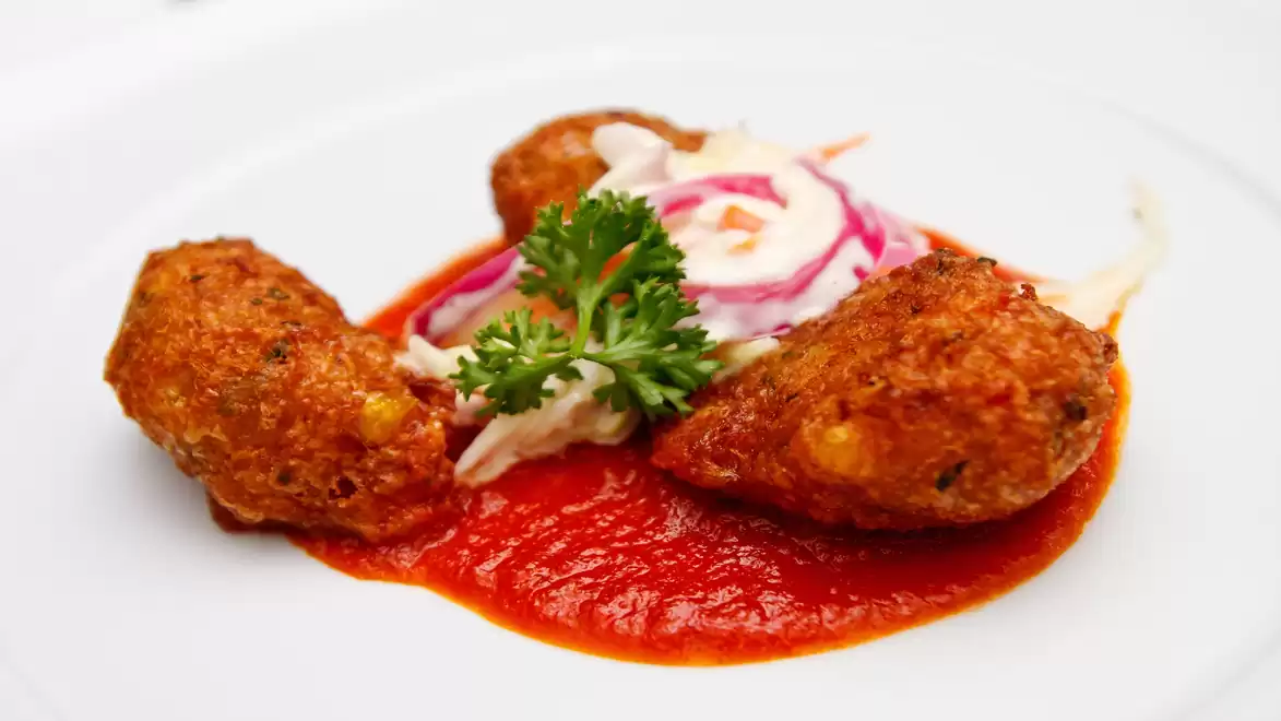 Close-up of three fried balls on red tomato sauce, garnished with parsley and a salad of red onions and cabbage.