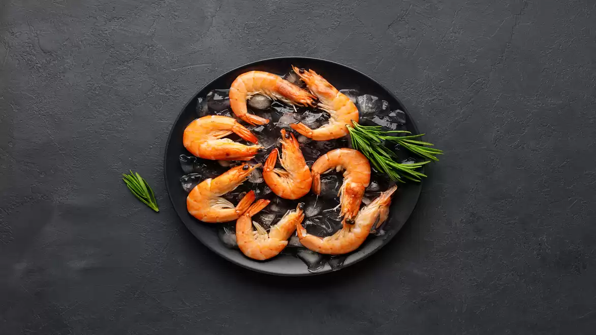 A black plate with grilled shrimp and rosemary on a dark background.