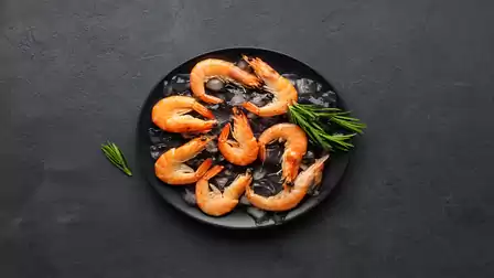 A black plate with grilled shrimp and rosemary on a dark background.