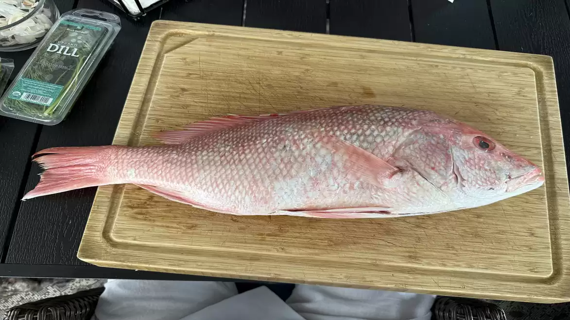 Fresh red fish on a wooden cutting board next to a pack of dill.
