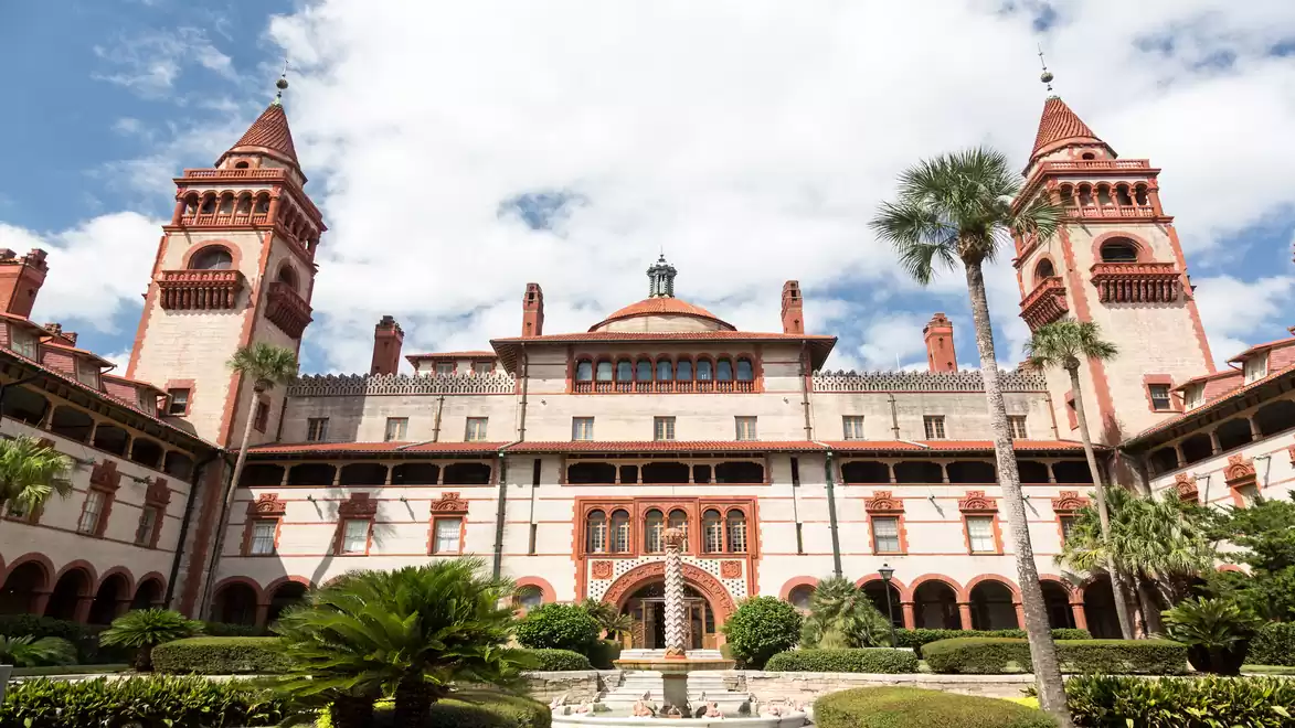 Historic building with towers and palm trees in the foreground, blue sky with few clouds.