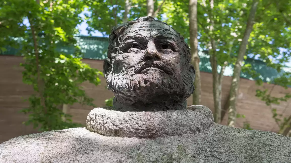 Close-up of a stone bust of a man in a green, wooded area.