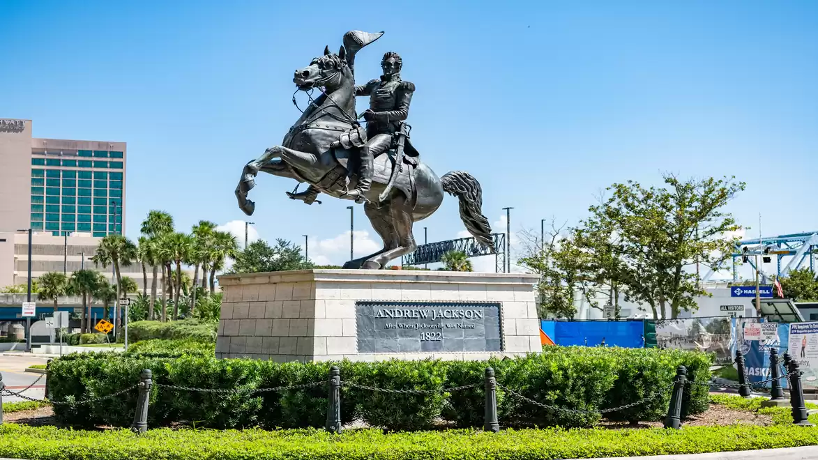 Equestrian statue in an urban setting with clear sky and green vegetation in the foreground.