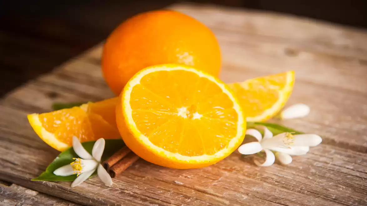 A fresh orange, halved and sliced, on a rustic wooden table with blossoms and a cinnamon stick.