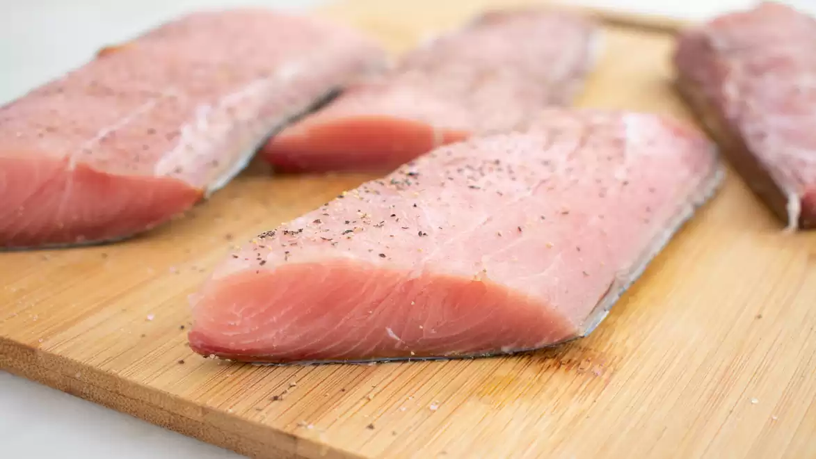 Fresh Mahi-Mahi fillets on a wooden board seasoned with pepper.