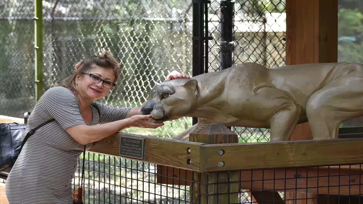 A woman poses next to a puma statue in a fenced outdoor area.