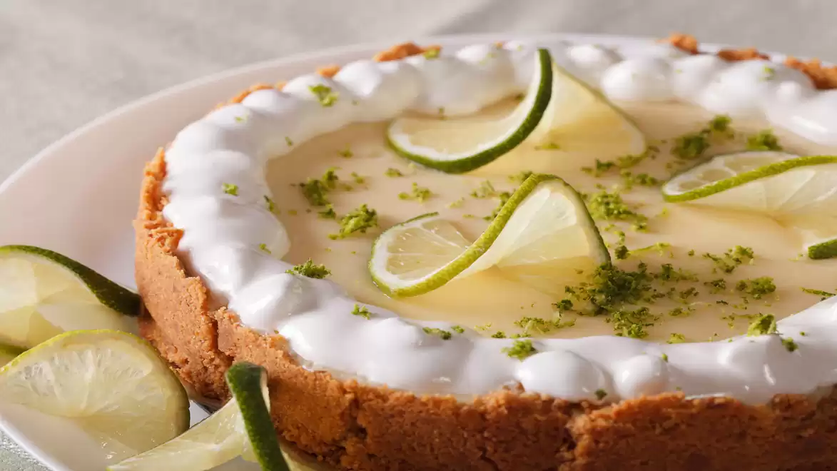 A delicious lime pie with a crispy crust, topped with lime slices and whipped cream, on a plate.